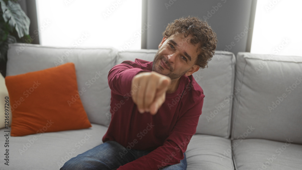 Young man pointing while relaxing on a sofa in a cozy, modern living room, showcasing a casual, friendly atmosphere indoors. Young man pointing while relaxing on a sofa in a cozy, modern living room, showcasing a casual, friendly atmosphere indoors.