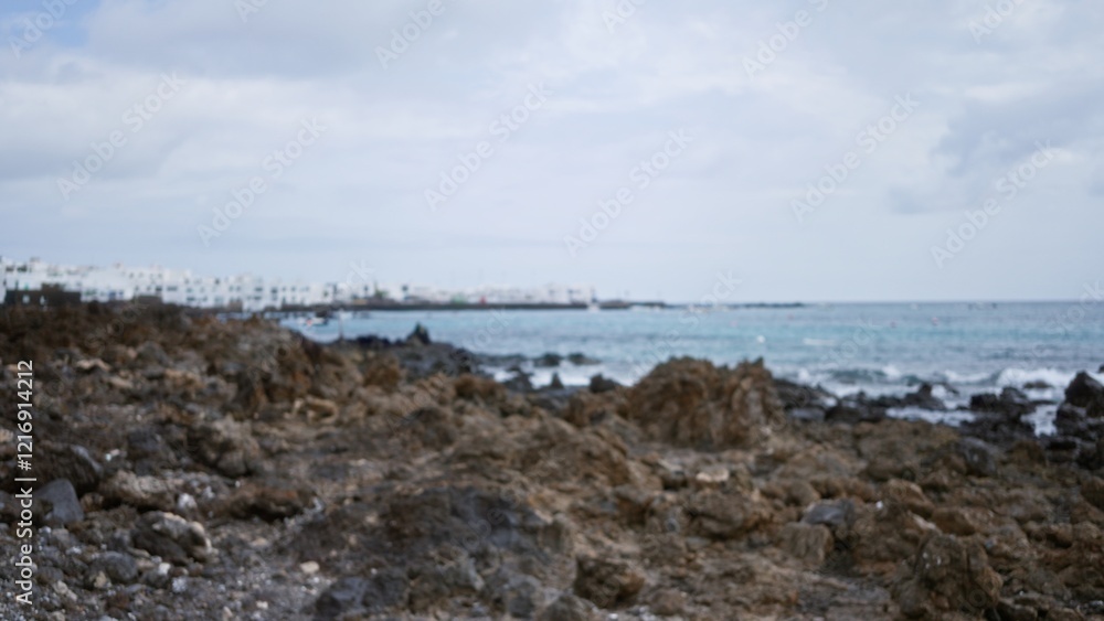 Blurred coastal scene on lanzarote in the canary islands, spain with rocky shores and distant buildings in an outdoor setting. Blurred coastal scene on lanzarote in the canary islands, spain with rocky shores and distant buildings in an outdoor setting.