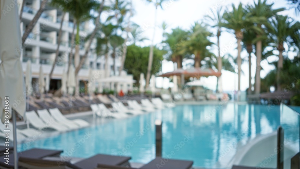 Blurred tropical resort pool area with palm trees and lounge chairs in the background, creating a vacation bokeh effect Blurred tropical resort pool area with palm trees and lounge chairs in the background, creating a vacation bokeh effect