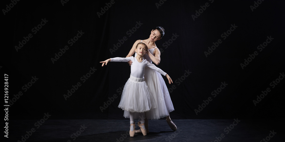 Adult ballerina guiding child in ballet posture, gently supporting arms, both dressed in white tutus, against black studio background. Concept of ballet, elegance and beauty, grace. Ad Adult ballerina guiding child in ballet posture, gently supporting arms, both dressed in white tutus, against black studio background. Concept of ballet, elegance and beauty, grace. Ad