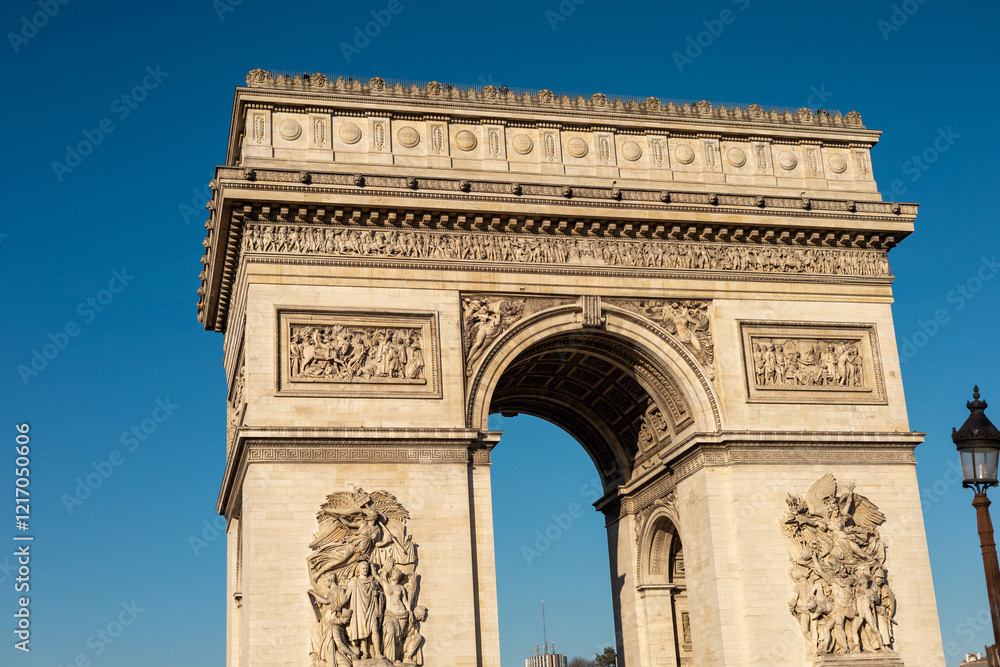 Fototapeta premium Visitors admire the impressive architecture of the Arc de Triomphe under clear blue skies in Paris