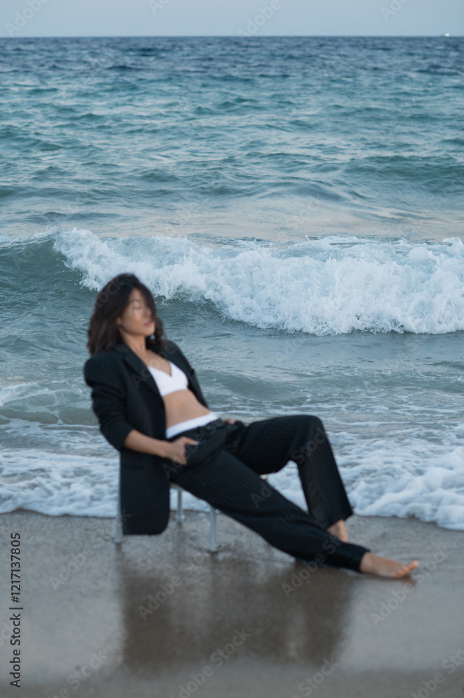 A young Asian woman sits on a chair in the water, wearing a suit with her hands in her pockets and eyes closed. The peaceful, reflective pose contrasts with the dynamic water around her. A young Asian woman sits on a chair in the water, wearing a suit with her hands in her pockets and eyes closed. The peaceful, reflective pose contrasts with the dynamic water around her.
