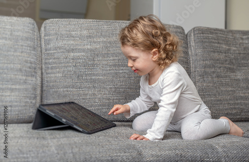 Obraz na płótnie Little girl using a tablet in a cozy home environment. A small child playing with a tablet in a comfortable home setting. w salonie