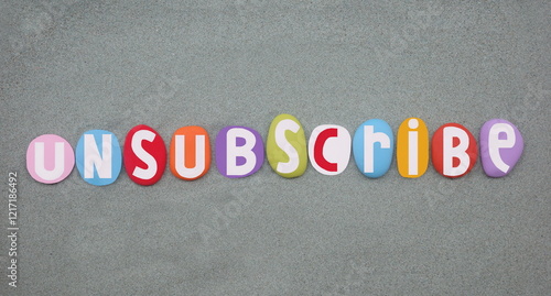 Unsubscribe, cancel a subscription to an electronic mailing list or online service, creative text composed with hand painted multi colored stone letters over green sand photo