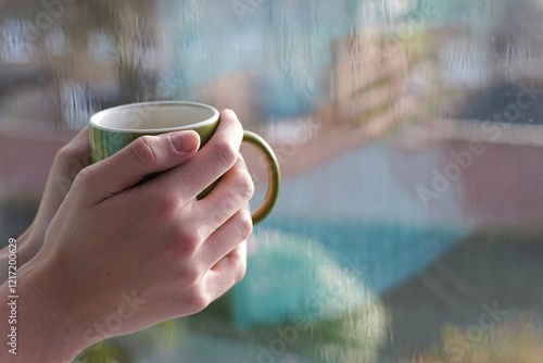 Man holding green cup near wet window