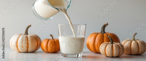 Pouring milk into a glass with pumpkins nearby. photo