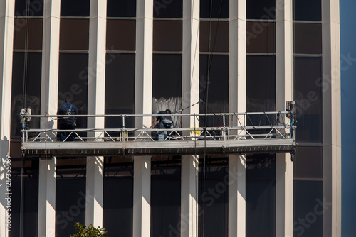 Window washers on scaffold on large commercial buildng with linear columns. There is soap on the window photo