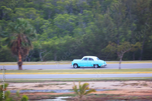 A vintage car drives along a country road on the Caribbean island of Cuba, Caribbean, Central America..