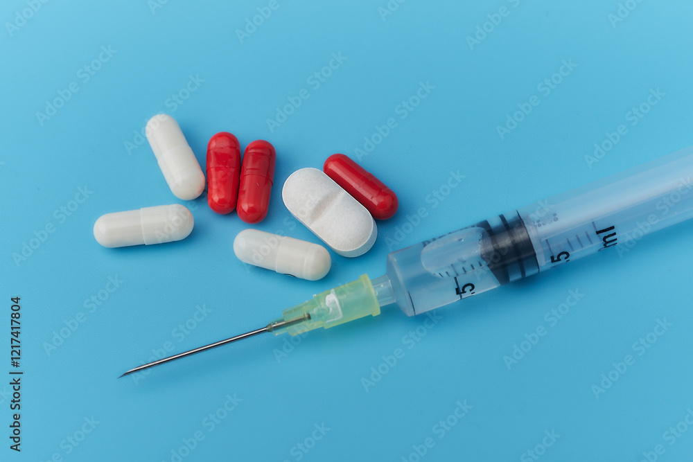 Close-up of a syringe and assorted red and white pills on a bright blue background. Ideal for illustrating healthcare, pharmaceuticals, and medical treatment concepts