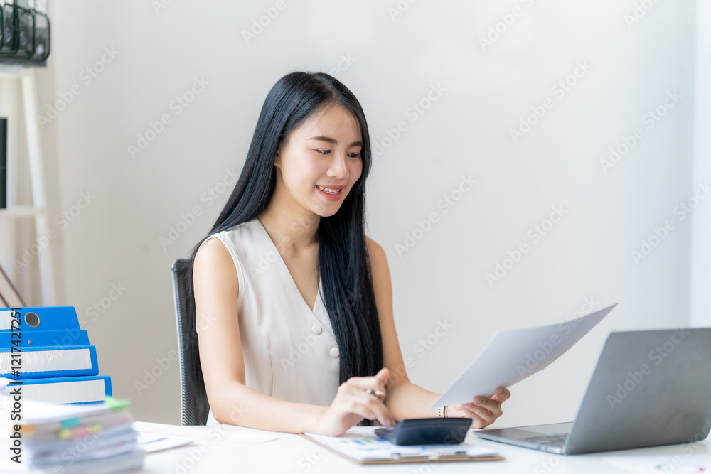 Focused Accountant: A young, smiling businesswoman sits at her desk, meticulously reviewing paperwork and using a calculator, showcasing professionalism and dedication in her work. Focused Accountant: A young, smiling businesswoman sits at her desk, meticulously reviewing paperwork and using a calculator, showcasing professionalism and dedication in her work.