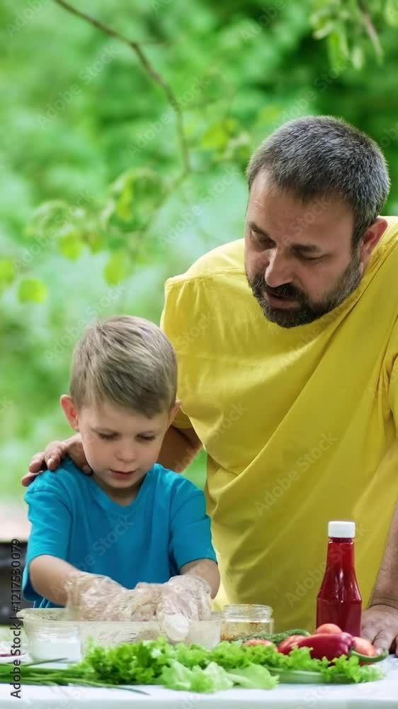 Dad and son marinating meat for grilling. Family picnic in the park. Dad and son marinating meat for grilling. Family picnic in the park.