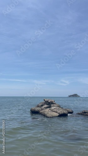A single rock and the beach horizon, with blue water, a clear sky, and a relaxing atmosphere.