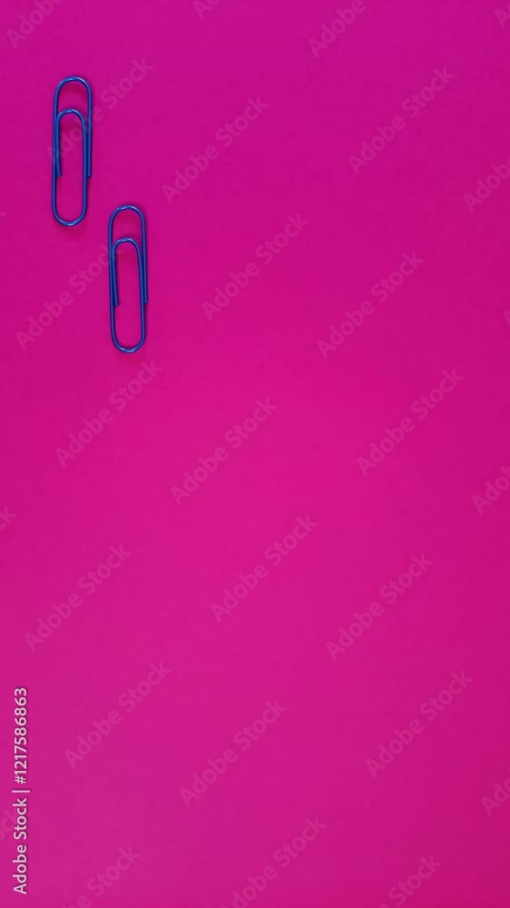 Step by step. Vertical Stop motion. Two blue paper clips are moving along the left edge of the pink surface. Looped video. Step by step. Vertical Stop motion. Two blue paper clips are moving along the left edge of the pink surface. Looped video.