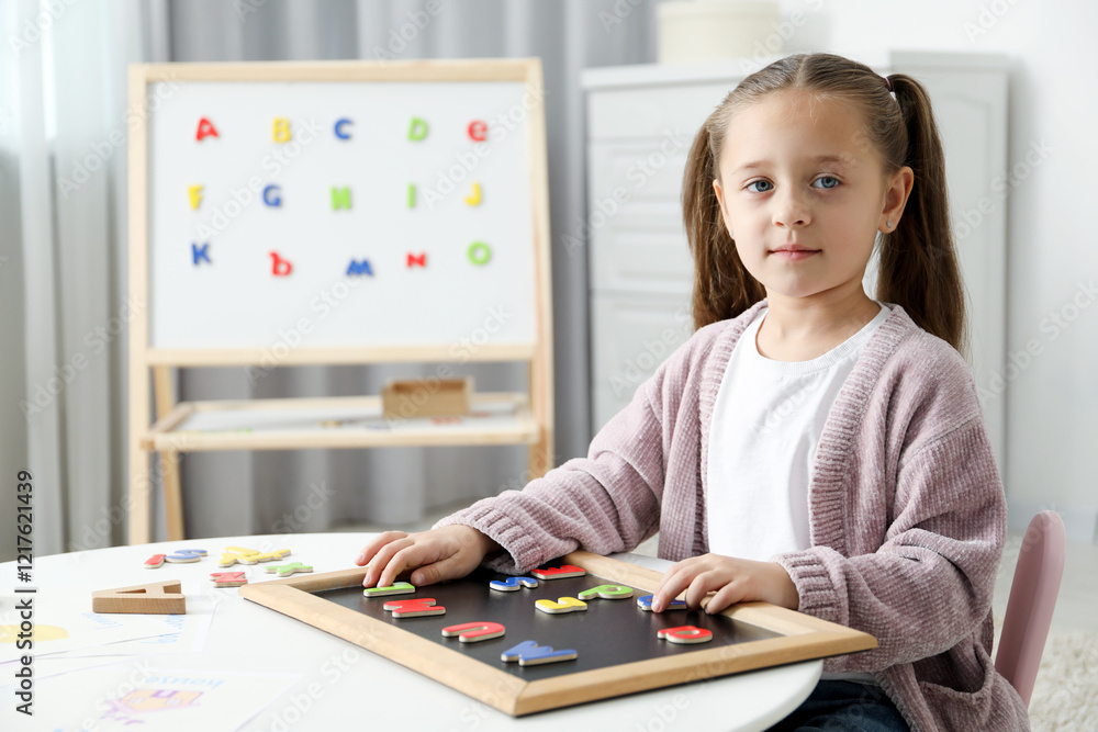 Little girl learning alphabet with magnetic letters at white table indoors Little girl learning alphabet with magnetic letters at white table indoors