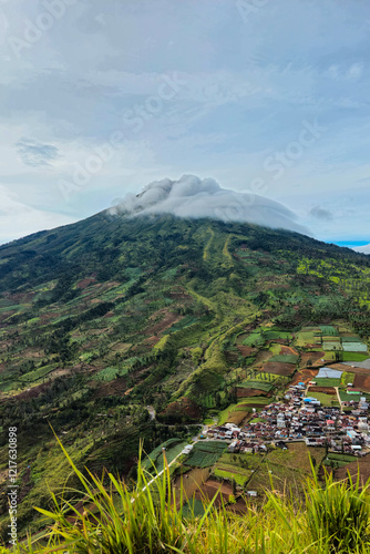 Landscape Mount Sindoro from a close distance with clouds around the peak on a sunny morning. The beautiful and green view of Mount Sindoro from the top of the hill at an altitude of 1800 mdpl photo