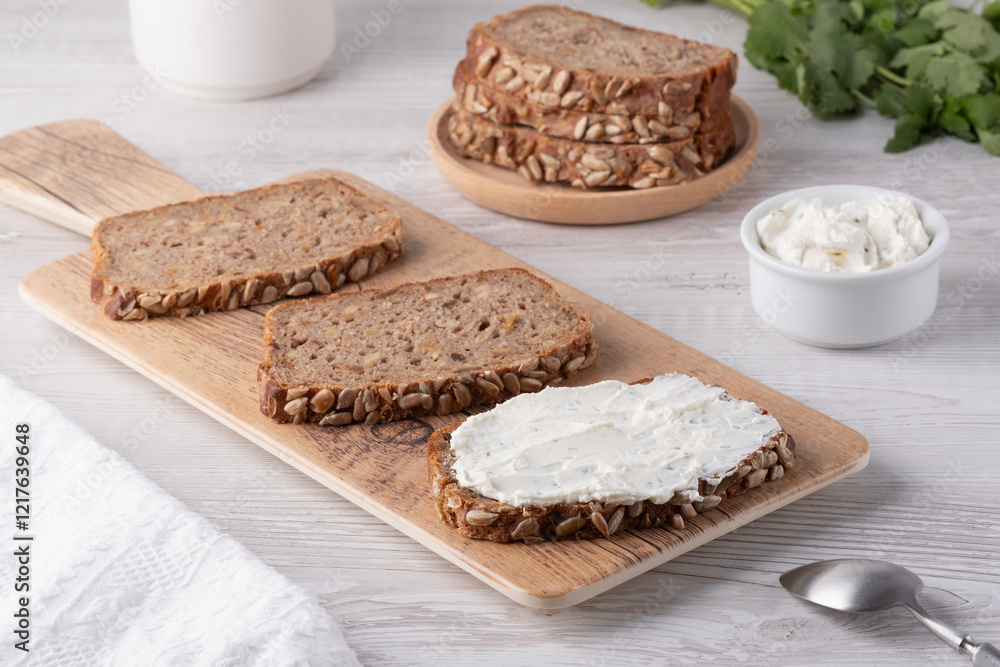 Slices of whole grain bread topped with cream cheese on a wooden cutting board in a cozy kitchen setting Slices of whole grain bread topped with cream cheese on a wooden cutting board in a cozy kitchen setting