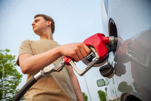 Selective focus view of a young man pumping gas into a silver vehicle