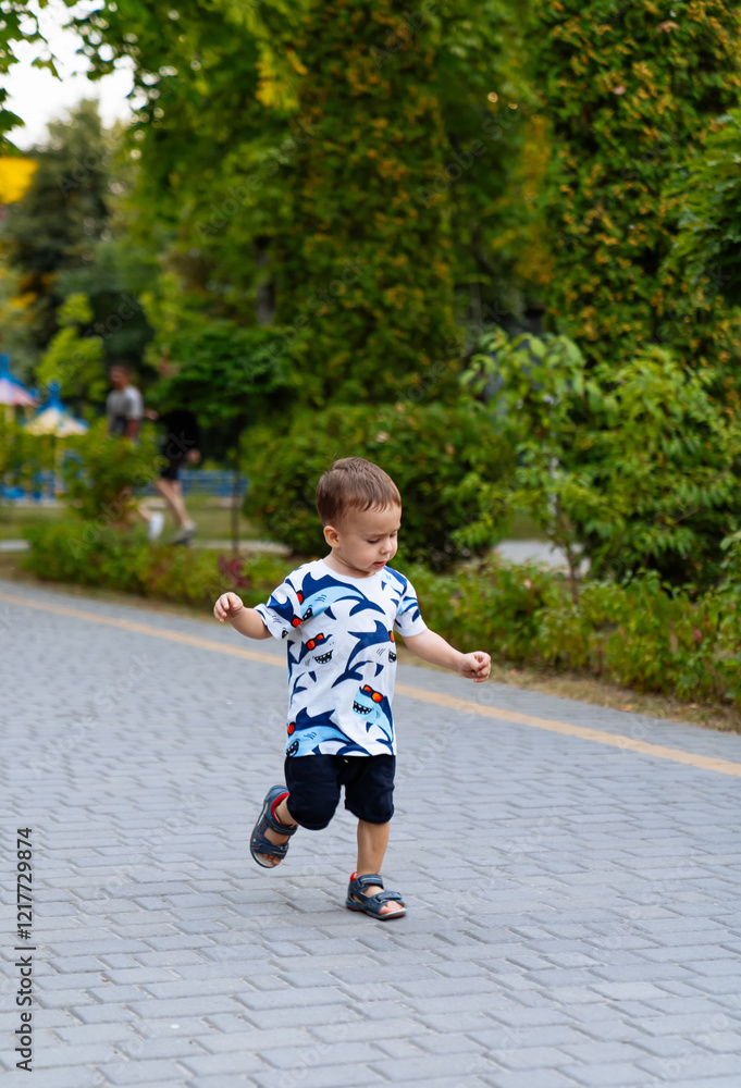 Child joyfully running in a green park. A young child in a playful shirt runs happily along a paved path in a lush park on a sunny day. Child joyfully running in a green park. A young child in a playful shirt runs happily along a paved path in a lush park on a sunny day.