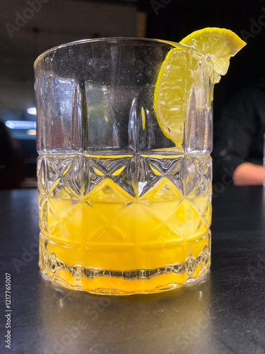 Image of a glass cocktail on a table, possibly a mimosa or Bloody Mary with citrus hue and garnish, in an indoor setting with warm lighting photo