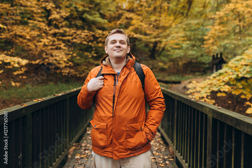 Obraz na płótnie 30s Plus size male with backpack smiling outside on an adventure. Hiking, lifestyle, adventure and tourism concept. Young man standing on the bridge in woodland, autumn time. w salonie