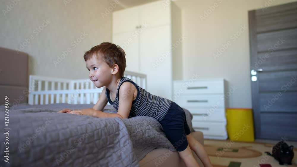 Beautiful Caucasian toddler child climbs off the big bed. Baby boy in the bedroom. Black cat sits on the floor. Beautiful Caucasian toddler child climbs off the big bed. Baby boy in the bedroom. Black cat sits on the floor.