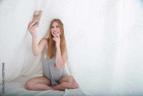 Sexy blonde woman takes selfie under sheets in bed photo