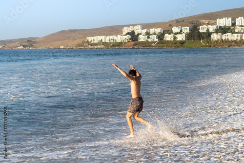 Obraz na płótnie A young man enthusiastically leaping into the sea to swim, with the warm hues of the sunset creating a serene and captivating backdrop w salonie