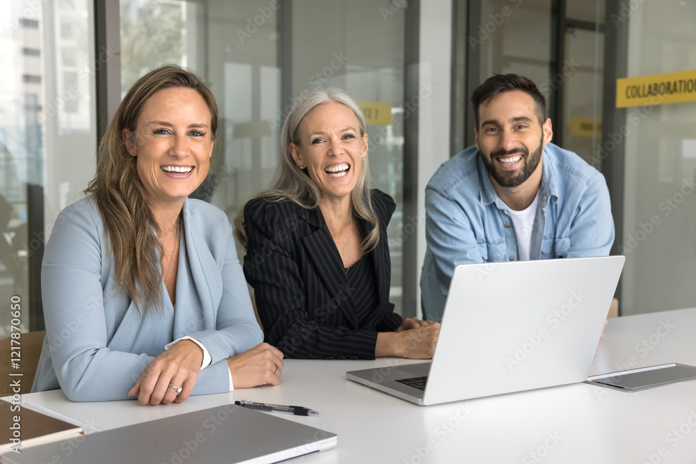 Fototapeta premium Portrait of happy skilled diverse teammates gather together in office, sit at conference table with laptop, take part in brainstorming or briefing session, laughing, look at camera. Synergy, teamwork