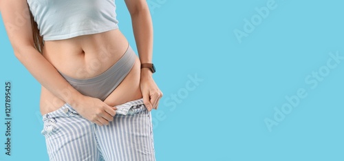 Young woman trying to put on tight pants against light blue background with space for text, closeup. Diet concept photo