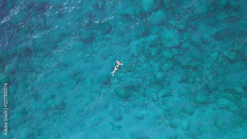 A young woman in a swimsuit lies in the sea during a summer vacation at a resort, aerial drone shooting from top to bottom