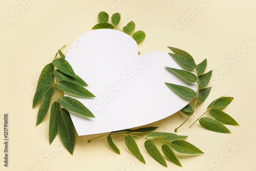 Blank heart shaped card and green plant leaves on color background photo