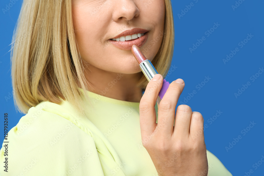 Woman applying lipstick against blue background, closeup Woman applying lipstick against blue background, closeup