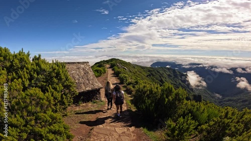 Active people with backpacks hiking trail path and climbing Pico Ruivo mountain in Madeira. Group of girlfriends enjoying summer vacation with beautiful view of clouds above the mountains