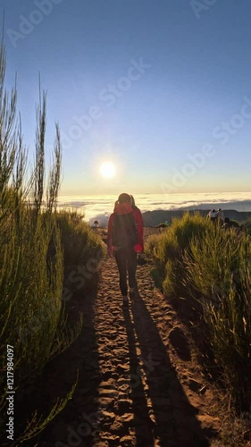 Active women with backpacks hiking trail path and climbing Pico Ruivo mountain with beautiful sunrise view and clouds on the sky. Group of girlfriends enjoying summer vacation in Madeira 