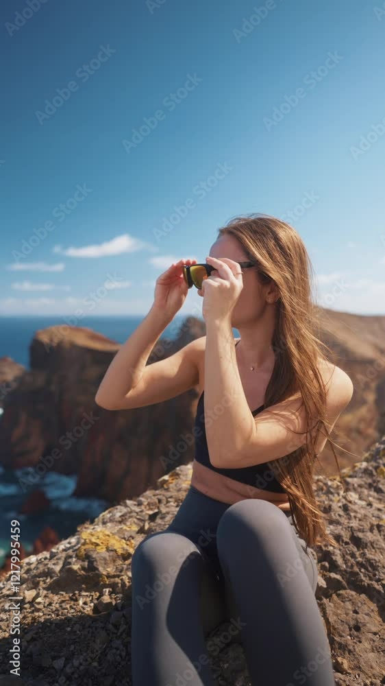 Vertical video of hiker woman sitting on the edge of epic rocky cliff coastline. Tourist active woman enjoying summer adventure journey in nature. Travel exploring Madeira Island Vertical video of hiker woman sitting on the edge of epic rocky cliff coastline. Tourist active woman enjoying summer adventure journey in nature. Travel exploring Madeira Island