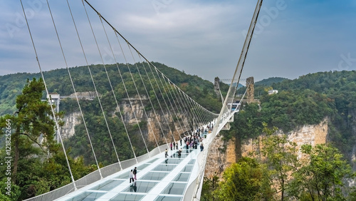 The longest glass suspension bridge in the world. People walk over a precipice on a transparent surface. Stretched support cables against the sky and rocks. China. Zhangjiajie Glass Bridge