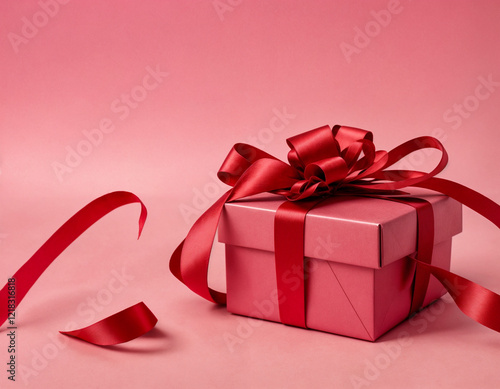 Valentine's Day flat lay composition with gift boxes wrapped in heart-patterned paper and red ribbons, surrounded by red flowers and heart-shaped decorations on pink background. Love, romance concept