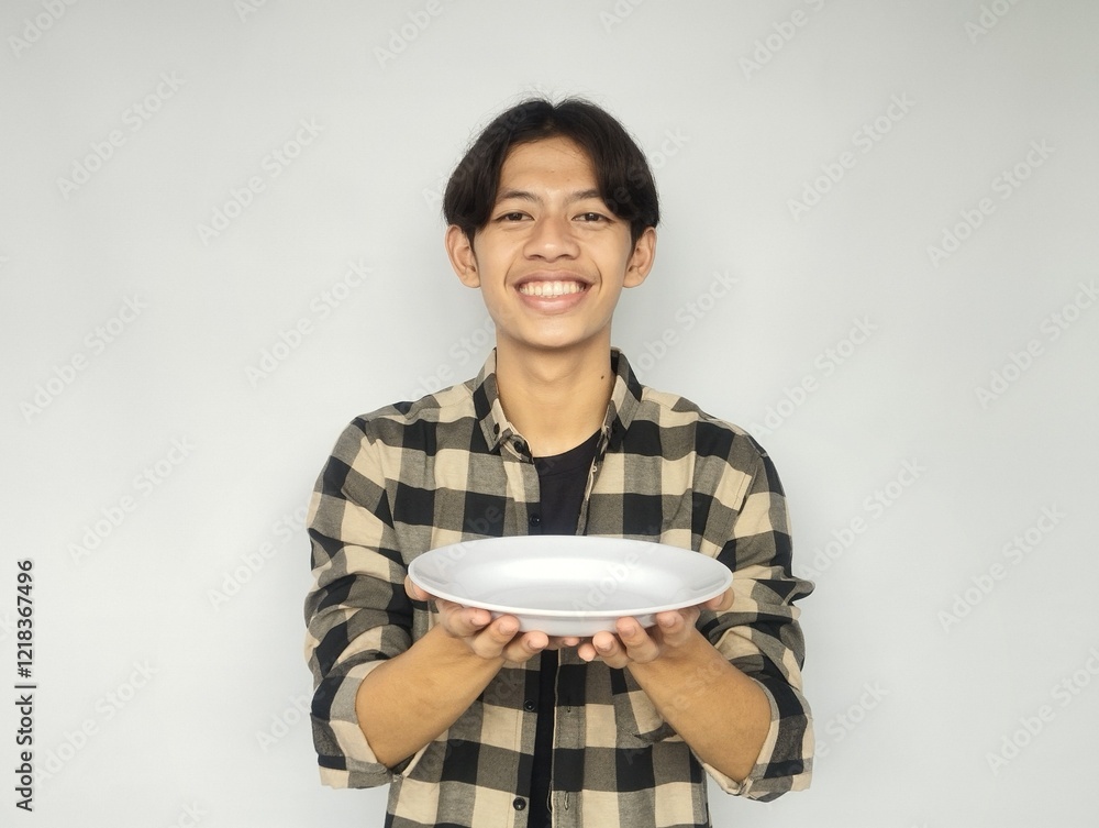 Young Asian man smiling happily while pointing at empty dinner plate Young Asian man smiling happily while pointing at empty dinner plate