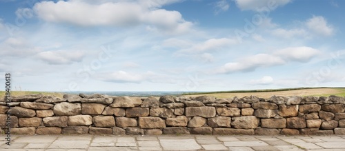 Panoramic view of an ancient stone wall under a bright blue sky with fluffy clouds, showcasing a serene landscape with rolling hills in the background.
