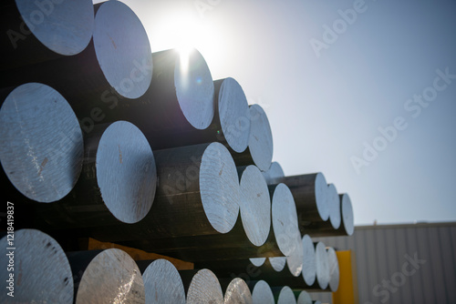 Fotografie Round aluminum billets stacked in a yard with sunlight lens flare