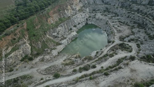 Green water has accumulated at the bottom of an abandoned quarry near sant fost de campsentelles, barcelona, surrounded by rocky terrain and vegetation photo