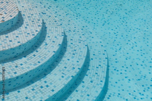 background with clear blue swimming pool water with mosaic tiles and stair steps in summer photo