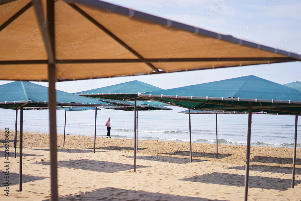 Beachfront Area with Empty Umbrellas and Lone Visitor by the Seashore Beachfront Area with Empty Umbrellas and Lone Visitor by the Seashore