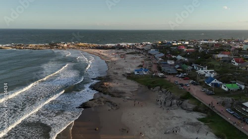 People and tourist parking at s Playa de los Pescadores in Punta del Diablo, Uruguay. Aerial rising wide shot. Sunset time with houses and home in town. photo