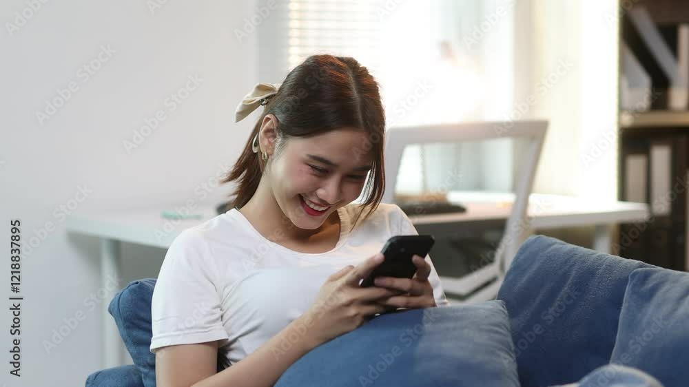 Young woman lounging on a blue couch, using a smartphone, she enjoys browsing social media and connecting with friends in a relaxed.