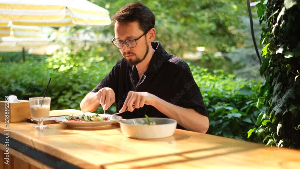 portrait of a young man with a beard eating cheesecakes with salad for breakfast on the terrace of a cafe on a sunny summer day portrait of a young man with a beard eating cheesecakes with salad for breakfast on the terrace of a cafe on a sunny summer day
