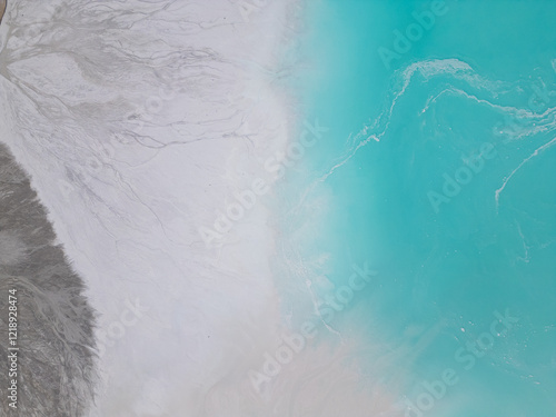 A turquoise tailings pond near a cement factory, surrounded by rugged hills. The vivid water contrasts with the barren land, creating a striking yet industrial scene of environmental impact photo