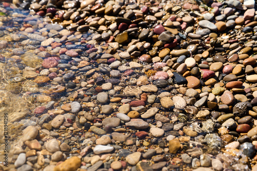 Colorful pebbles in clear water create a serene atmosphere at a riverside during sunny weather photo