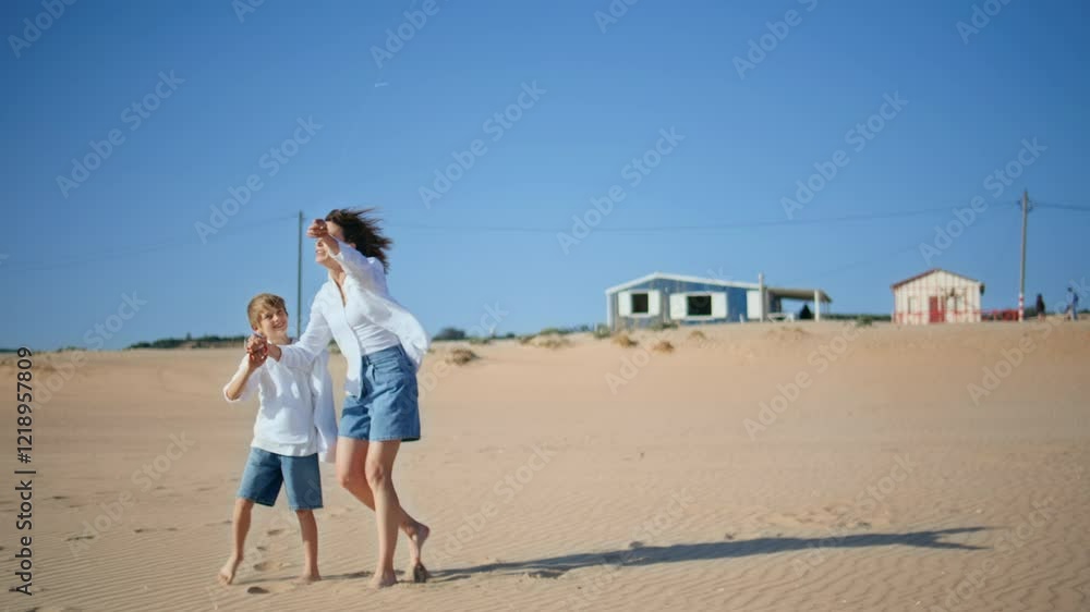 Woman son launching kite on breezy sandy beach. Energetic mother child playing Woman son launching kite on breezy sandy beach. Energetic mother child playing