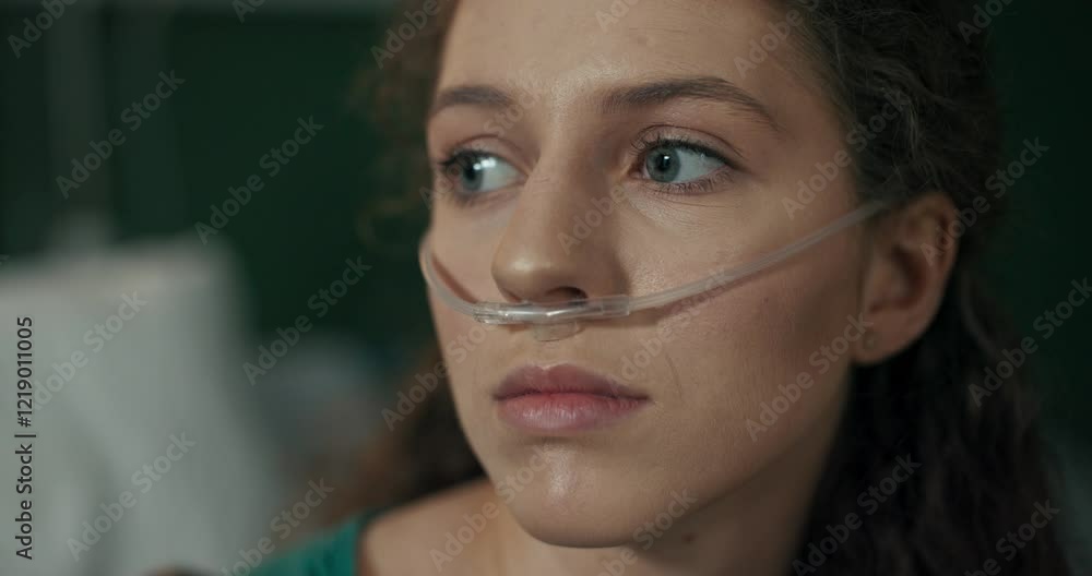 Young patient sits on her hospital bed, gazing ahead with determination, an oxygen tube in her nose. Young patient sits on her hospital bed, gazing ahead with determination, an oxygen tube in her nose.